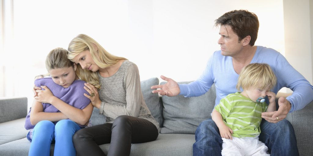 Mother consoling daughter as father sits with son on sofa